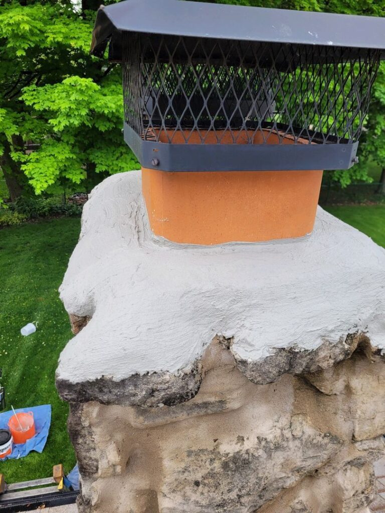 A chimney with a new white crown coat and black mesh cap, surrounded by trees.