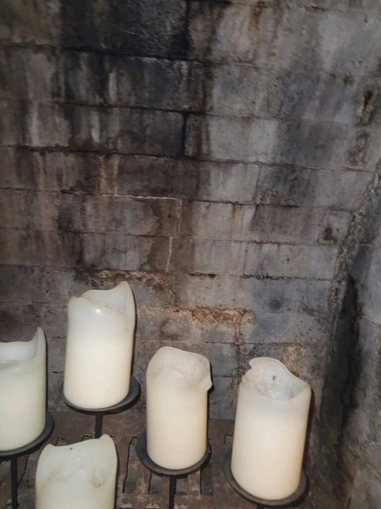 Interior view of a fireplace showing water stains on the brick wall and several unlit candles on a stand.