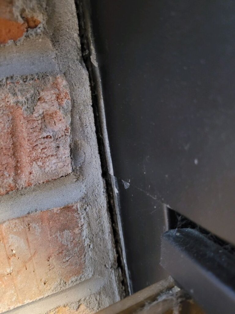 Image showing a gap between a black prefab firebox and red brick wall with mortar.