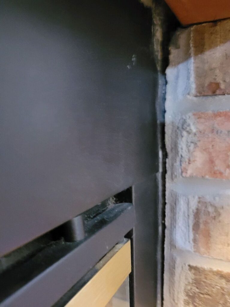 Close-up image of a gap between a black metal firebox and adjacent brickwork.