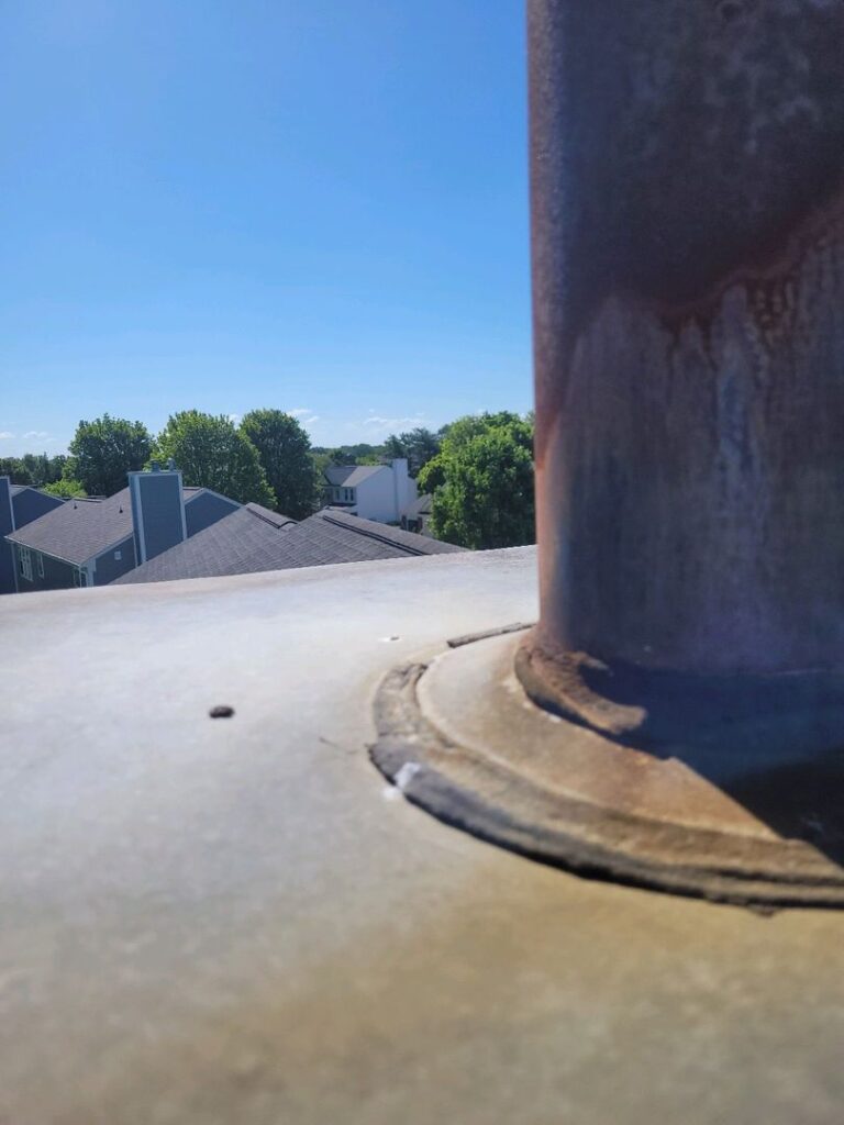 Top of a rusty chimney stack on a house roof with clear blue sky in the background