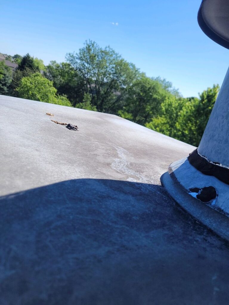 Deterioration and rust visible on a rooftop chase cover with a clear blue sky and greenery in the background