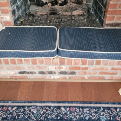 Brick fireplace with soot, two striped cushions in front, and a floral-patterned rug on hardwood floor