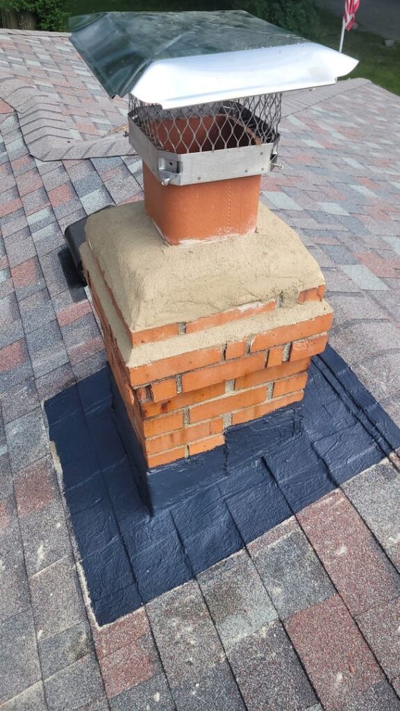 Brick chimney with metal cap on a shingled roof with an American flag in the distance