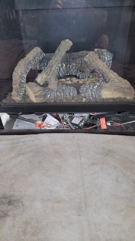 An open gas fireplace with artificial logs and maintenance tools and parts on the floor in front.