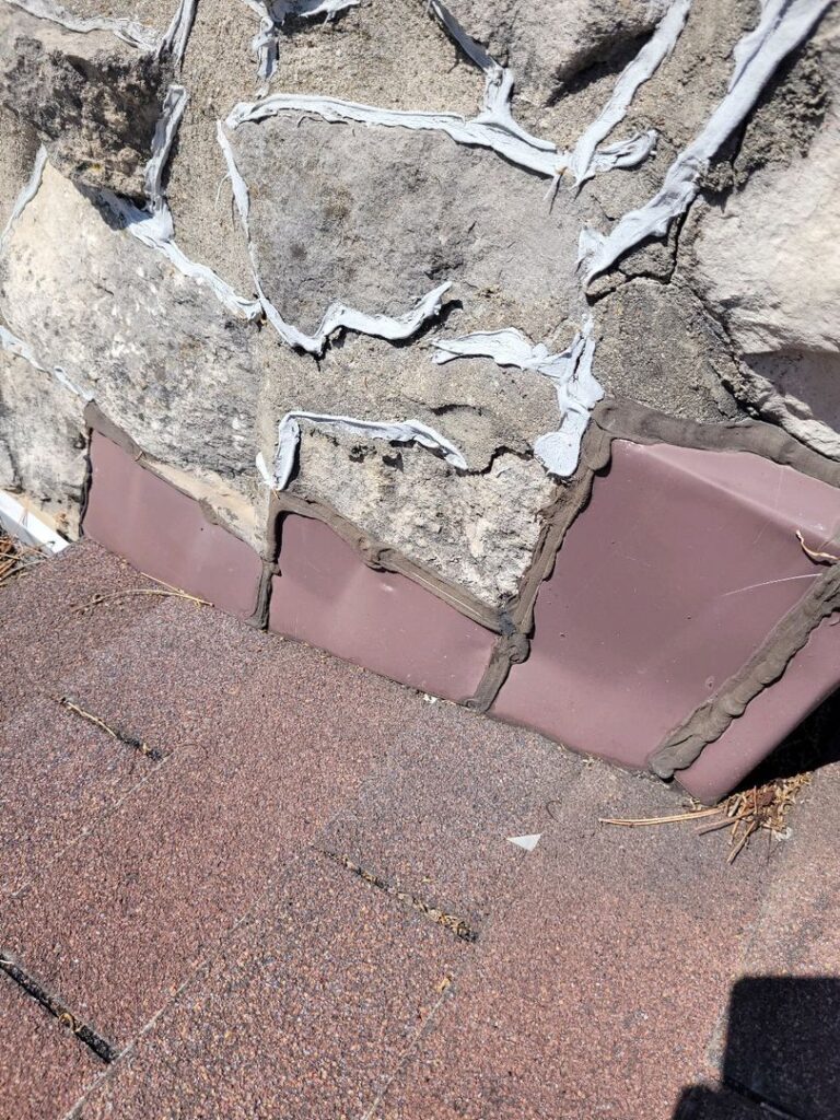 Close-up image showing where a stone wall meets a reddish-brown shingled surface with some wear and debris.