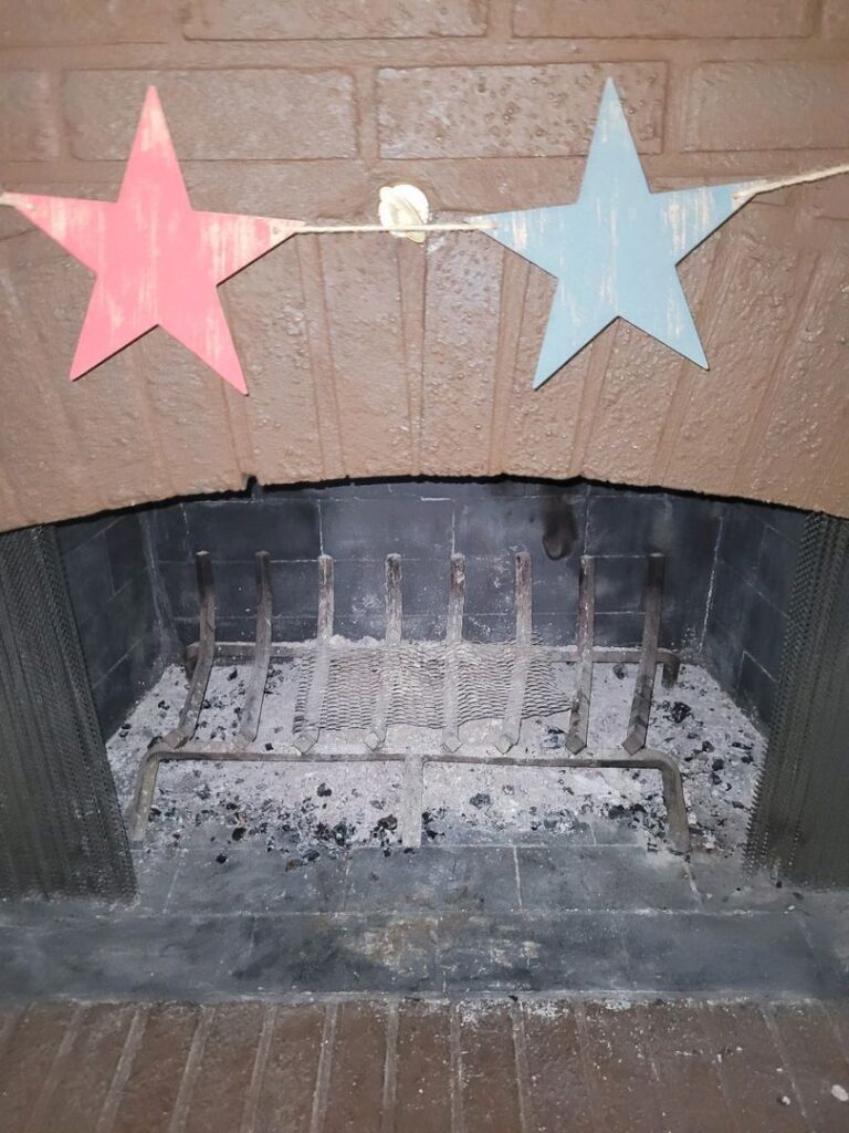 A brick fireplace with a metal grate, decorated with hanging pink and blue paper stars