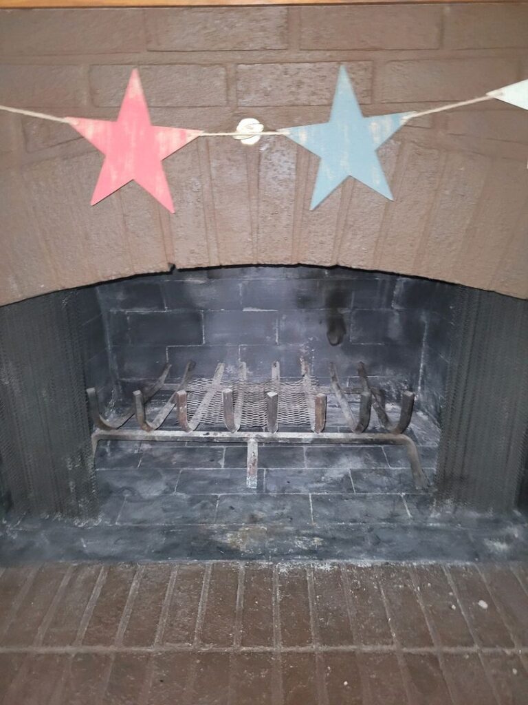 An empty brick fireplace with a metal grate, decorated with red and blue paper stars on a string.