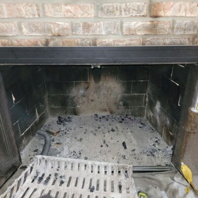 Ash-filled fireplace with cleaning tools including a brush and cordless drill on the hearth