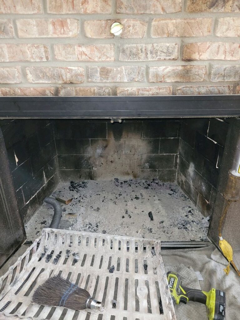 Ash-filled fireplace with cleaning tools including a brush and cordless drill on the hearth