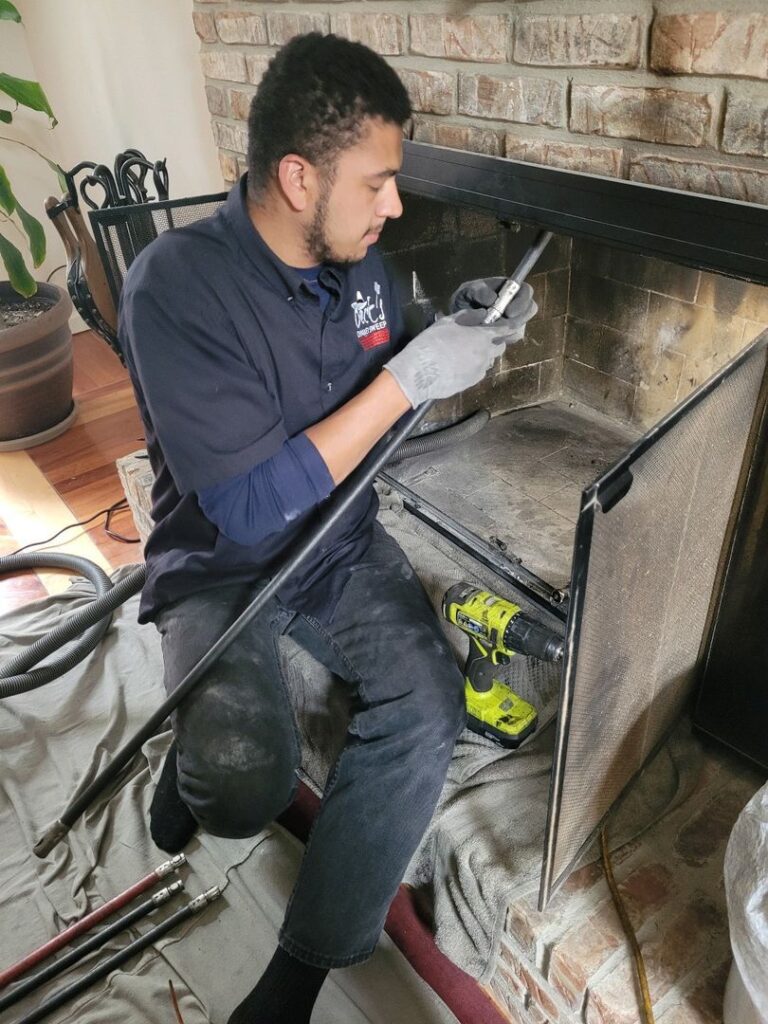 Technician in uniform cleaning and maintaining a residential fireplace with tools laid out on protective cloth.