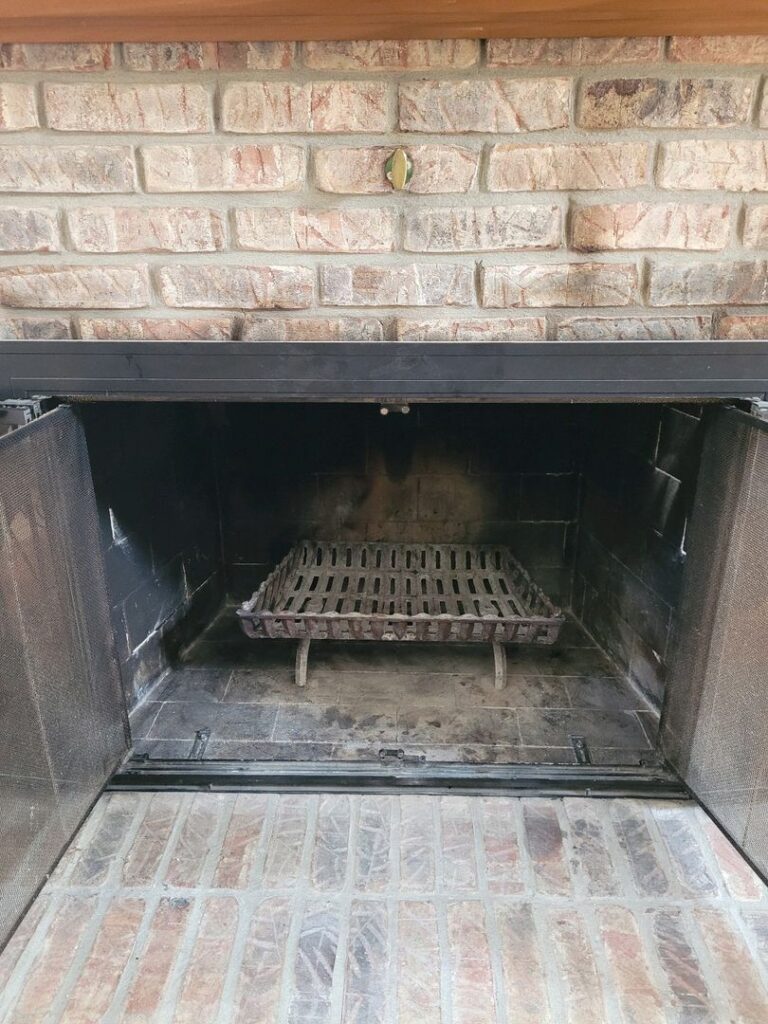 Interior view of a clean brick fireplace with an empty metal grate and no fire.