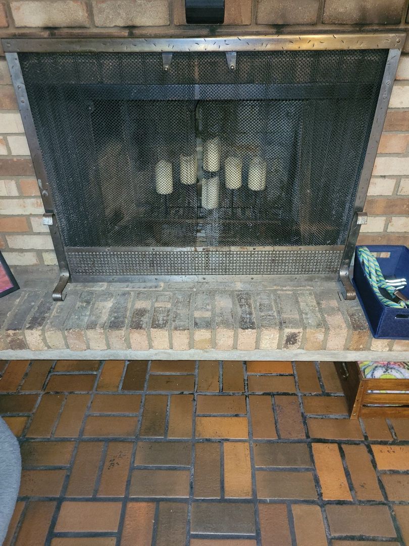 Brick fireplace with unlit white candles and an open metal mesh screen on a patterned tile floor