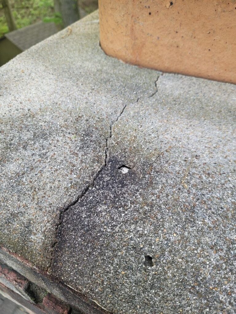 Image of a cracked concrete surface on top of a chimney, indicating possible structural issues