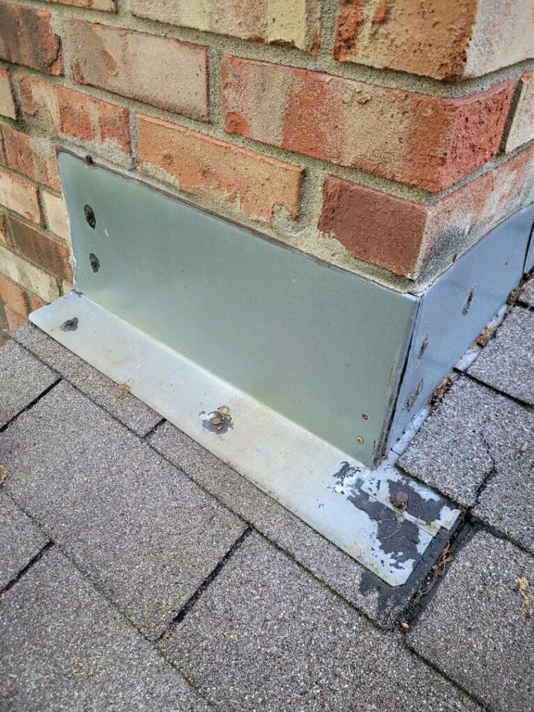 Close-up view of rusty metal flashing on a brick wall with peeling white paint at the base.