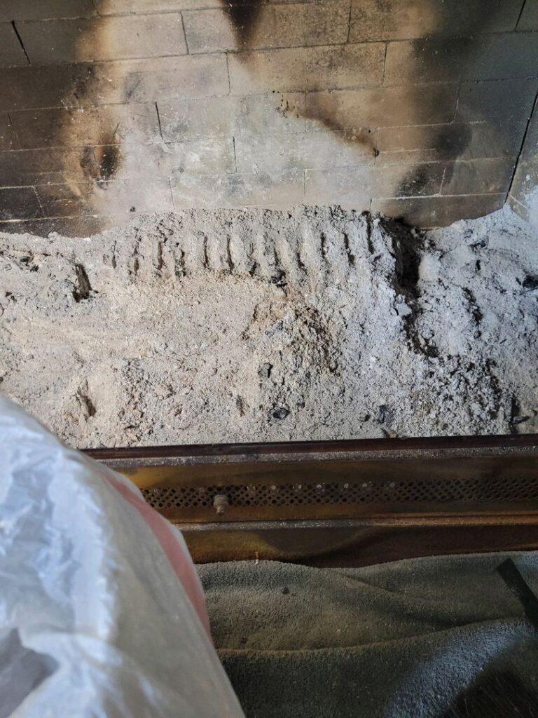 Interior view of a dirty fireplace showing ashes and soot on its base and walls.