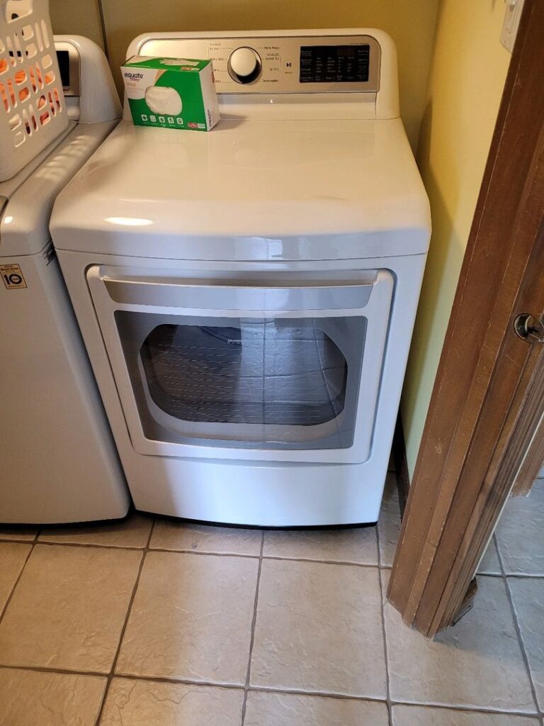 White front-loading dryer with a box of dryer sheets on top in a tiled laundry room.