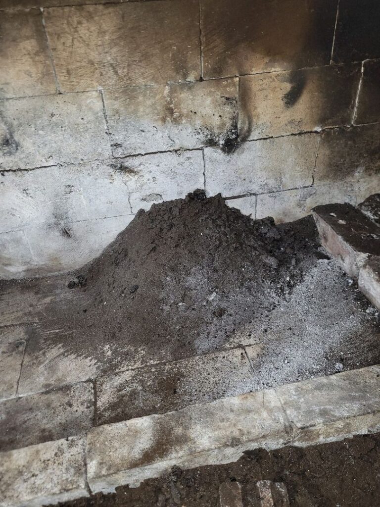 A pile of ash in the corner of a brick fireplace showing signs of use.