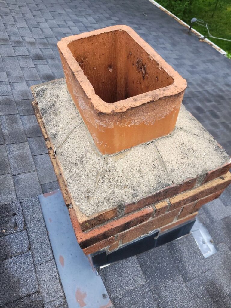 A close-up photo of a damaged chimney crown and open flue on a house roof.