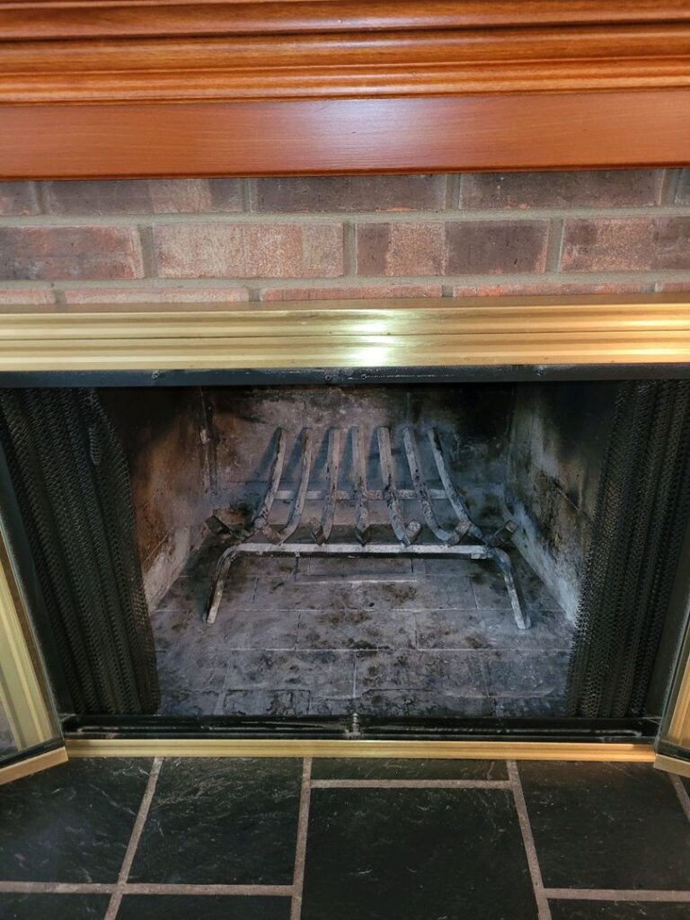 Clean interior of a brick fireplace with metal grate, surrounded by wood and tile