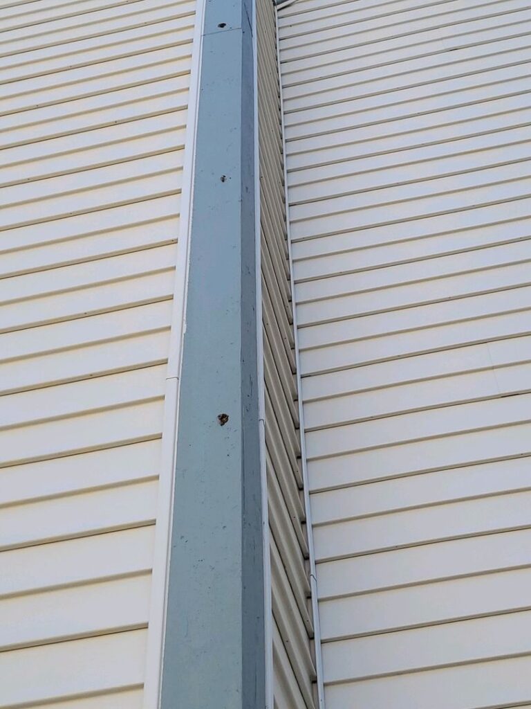 Close-up of a light blue metal downspout on cream-colored horizontal vinyl siding