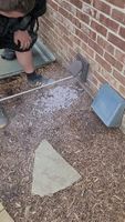 A pile of lint on the ground next to a brick wall with part of a person's body showing they are performing dryer vent cleaning.