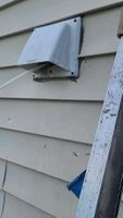 A metal dryer vent with a connected tube on the weathered siding of a building.