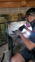 Technician in safety mask working on cleaning or repairing a home fireplace firebox