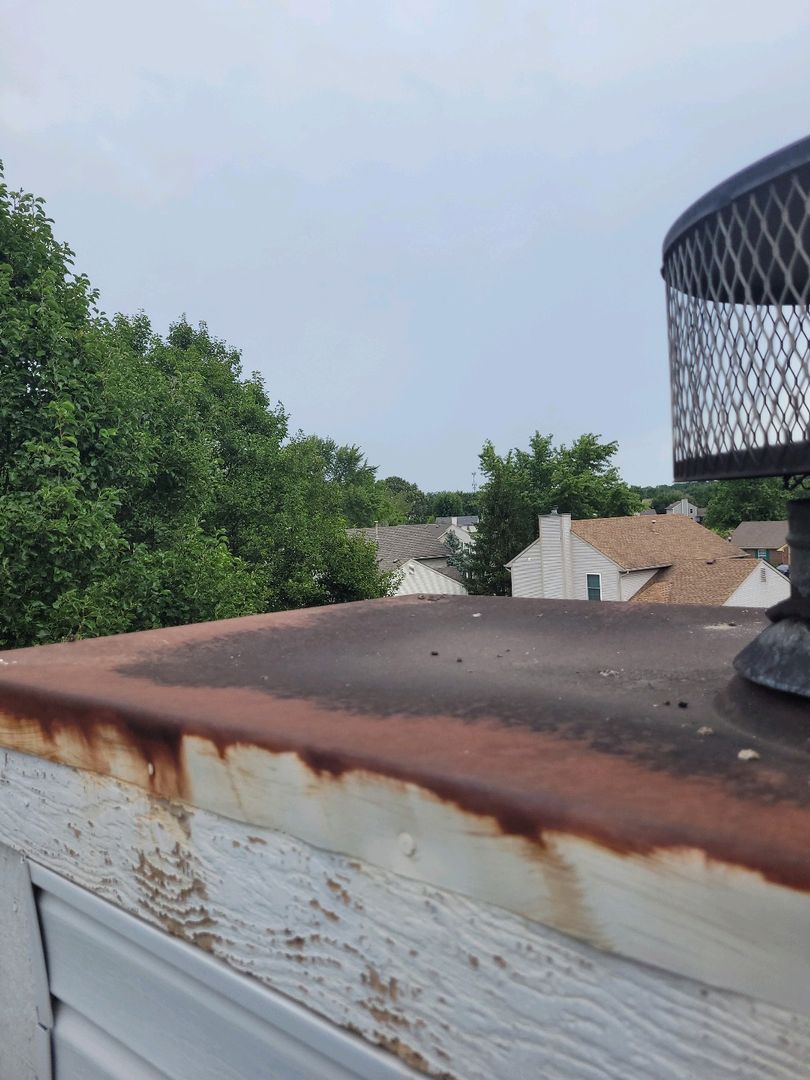 Rusted chase cover on top of a white structure with residential houses and trees in the background.