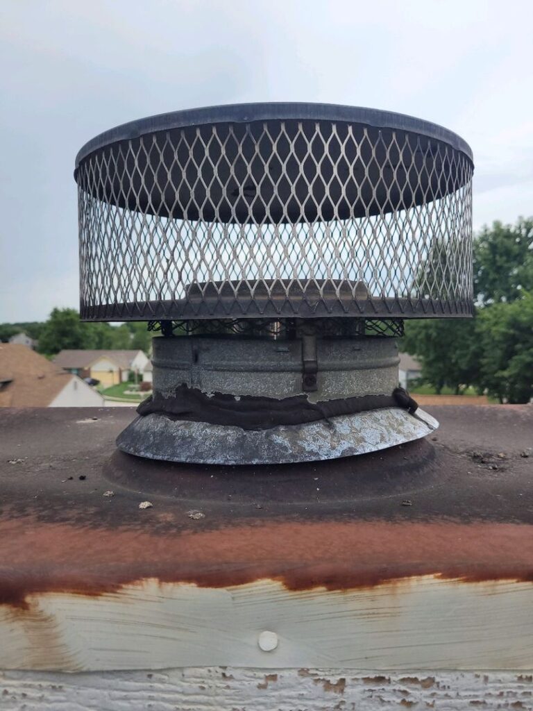 Close-up of a worn metal chimney cap with visible rust on the mounting surface.