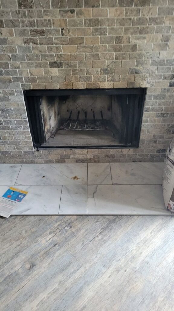 Image of a brick fireplace with a marble-tiled hearth and wooden flooring.