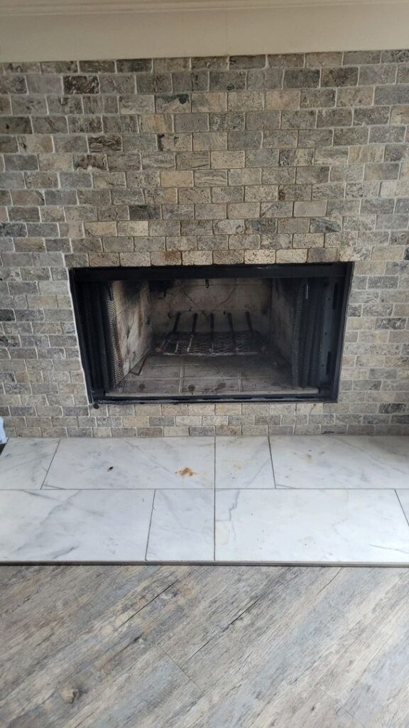 Brick fireplace with a black metal frame, marble hearth, and wooden floor.